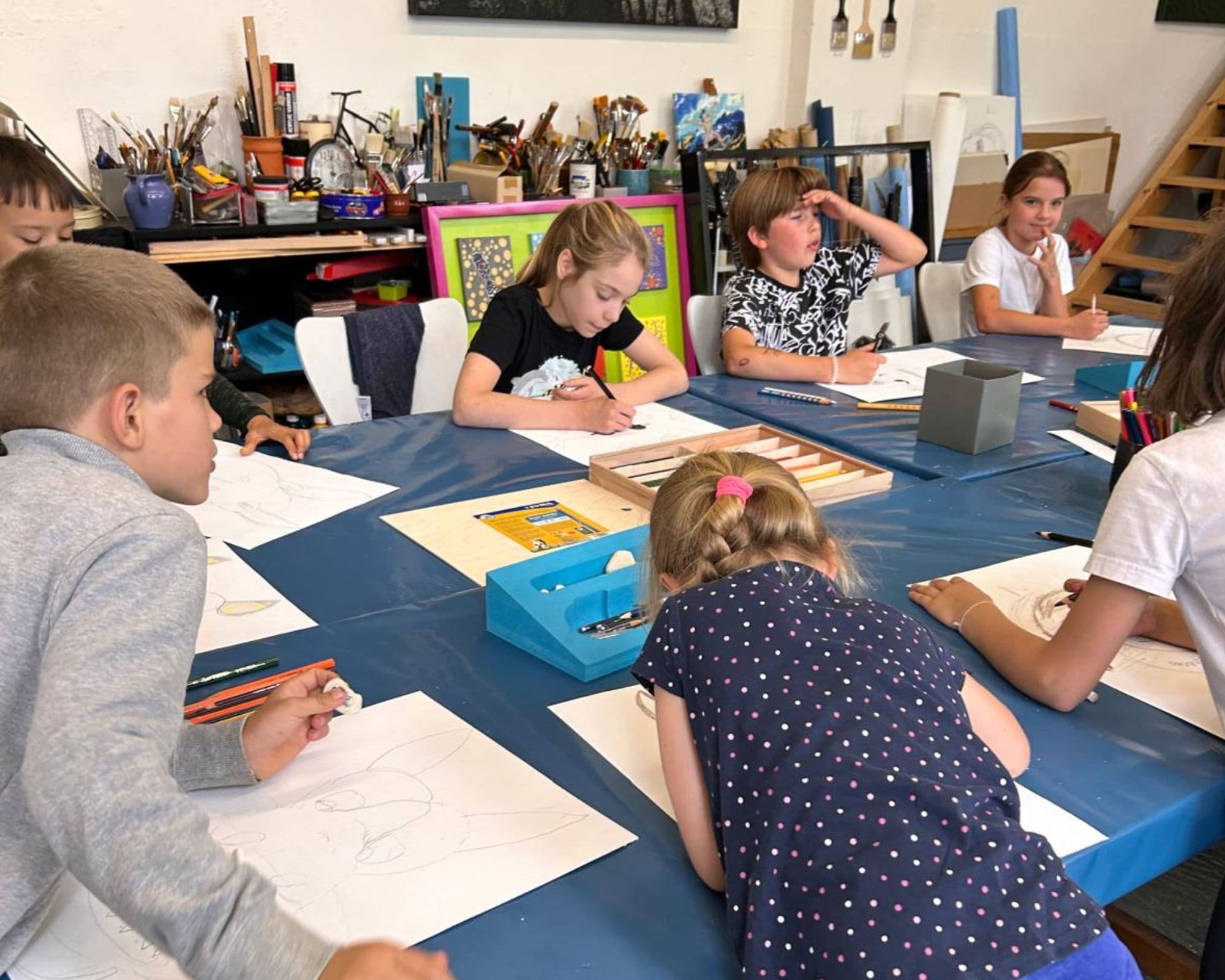 Kinder sitzen am Tisch und zeichnen auf Blöcken.