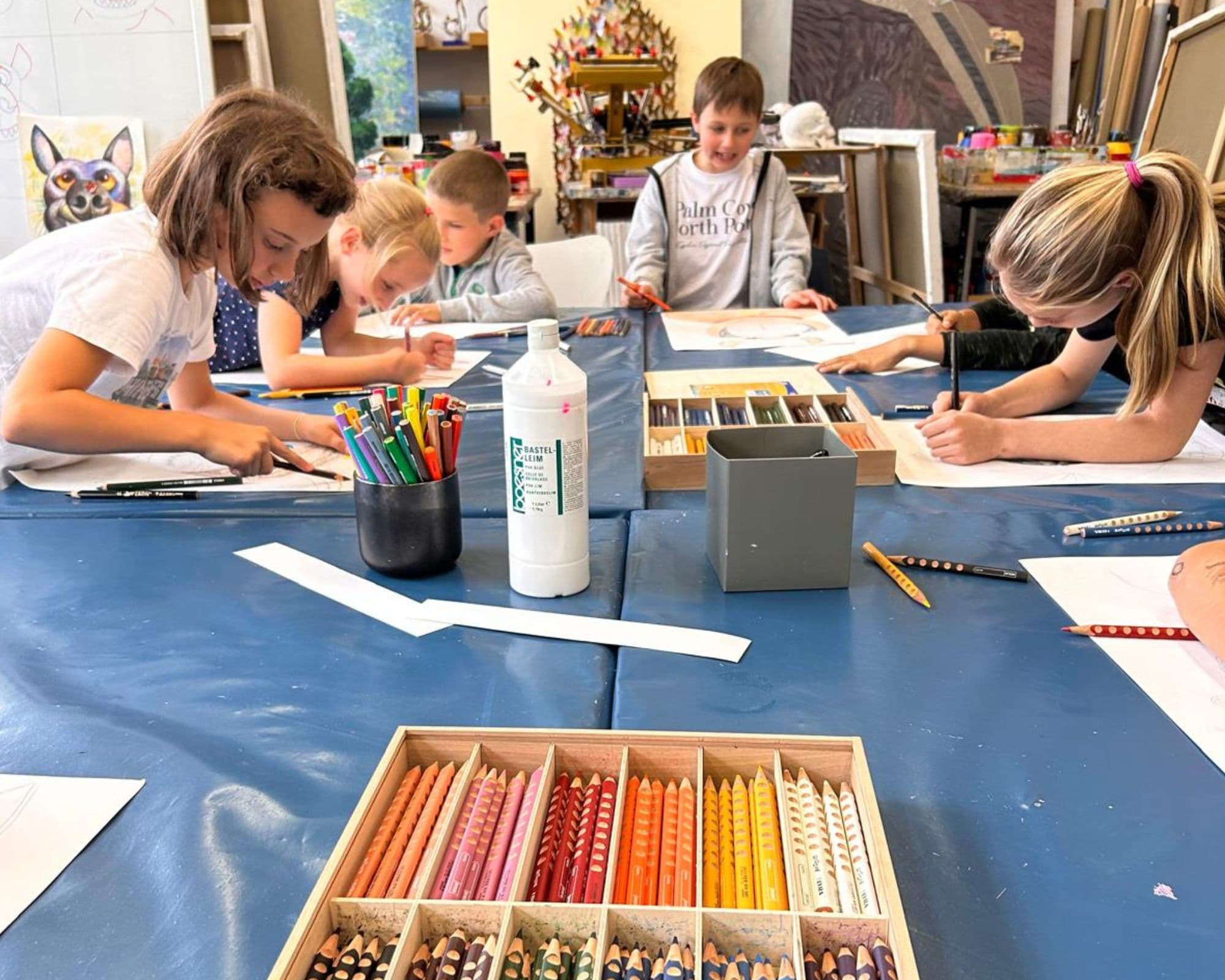 Kinder sitzen am Tisch und zeichnen mit bunten Stiften.